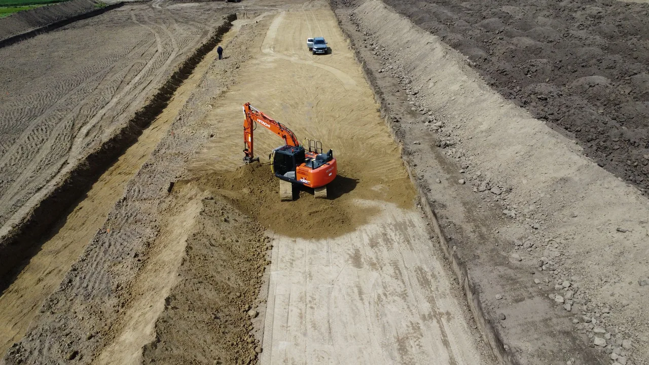 Blick von oben auf Aushubarbeiten für ein Bewässerungsbecken mit Bagger im Becken