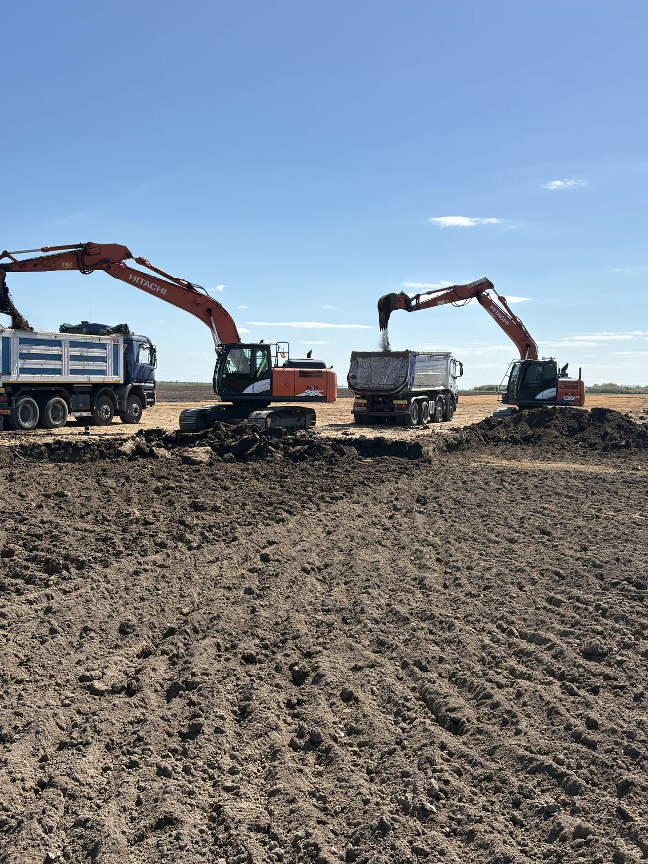 Două excavatoare Hitachi încărcând pământ în autobasculante pe un șantier Beavers